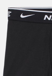 Pantaloncini da atleta neri con texture liscia, caratterizzati da una fascia larga in vita che mostra il logo Nike e una striscia bianca a contrasto.