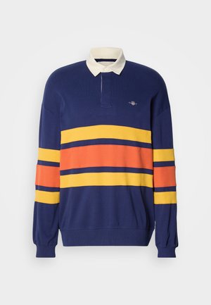 Polo-shirt à manches longues bleu marine avec un col blanc contrastant. Présente de larges rayures horizontales en jaune, orange et bleu marine sur la poitrine et les manches.