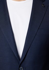 Granatowa marynarka z delikatnym wzorem w kratkę, z pojedynczym zapięciem na guzik i klapami, nałożona na białą koszulkę.