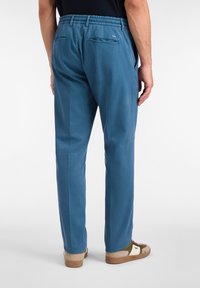 Blaue, lässig geschnittene Hose mit elastischem Bund, zwei Gesäßtaschen, glatter Textur und schmal zulaufenden Beinen. Getragen mit lässigen Turnschuhen.