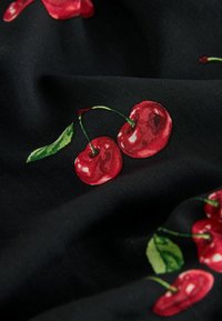 Černá tkanina s vzorem lesklých červených třešní se zelenými listy, vytvářející živý kontrast barev a designu.