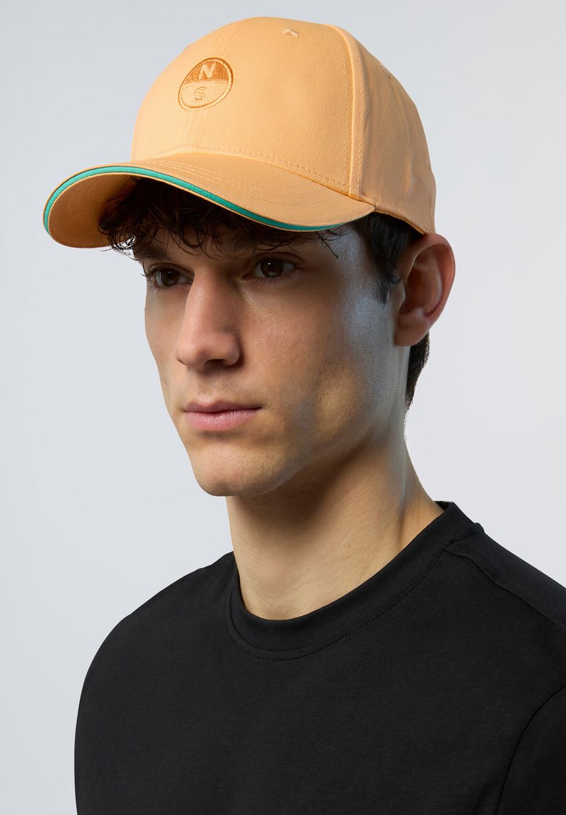 Cappello arancione con visiera curva, caratterizzato da un logo circolare sul davanti e un accento verde lungo la visiera. Texture del tessuto liscia.
