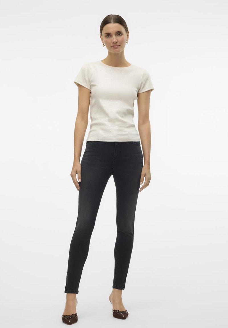 Crème kleurige t-shirt met korte mouwen in combinatie met zwarte skinny jeans. Het model draagt bruine ballerina's met een decoratief detail. Eenvoudig en slim fit ontwerp.