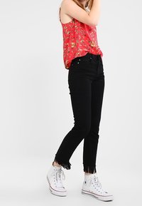 Rød blomstertrykt tanktop med tynde stropper, parret med højtaljede sorte jeans med frynset kant og hvide højhælede sneakers.