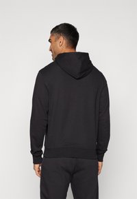 Sweat à capuche noir avec des manches longues, des poignets et un ourlet côtelés. Tissu doux avec une texture lisse. Design simple, sans logos ni motifs visibles.