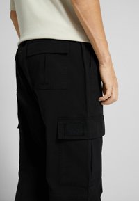 Svarta cargoshorts i lättviktsmaterial, med flera fickor, en platt midja och synliga sömmar.