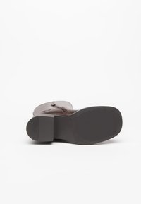 Stivale in pelle marrone con tacco a basso blocco, suola in gomma texture e zip laterale. Presenta una parte superiore liscia con dettagli minimi.
