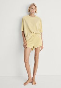 Gele katoenen t-shirt met korte mouwen en bijpassende shorts. De stof lijkt zacht, met een relaxte pasvorm. Eenvoudig ontwerp, geen zichtbare patronen of accenten.
