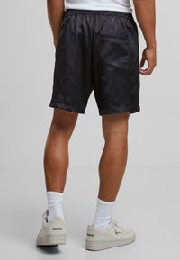 Sorte satin shorts med en elastisk talje, en baglomme og en glat struktur, parret med hvide sokker og lyse sneakers.