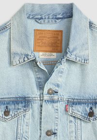 Svete modra denim jakna s klasičnim krojem, opremljena z usnjenim oznako, kovinskimi gumbi in dvema žepoma na prsih. Na oznaki je označena velikost M.