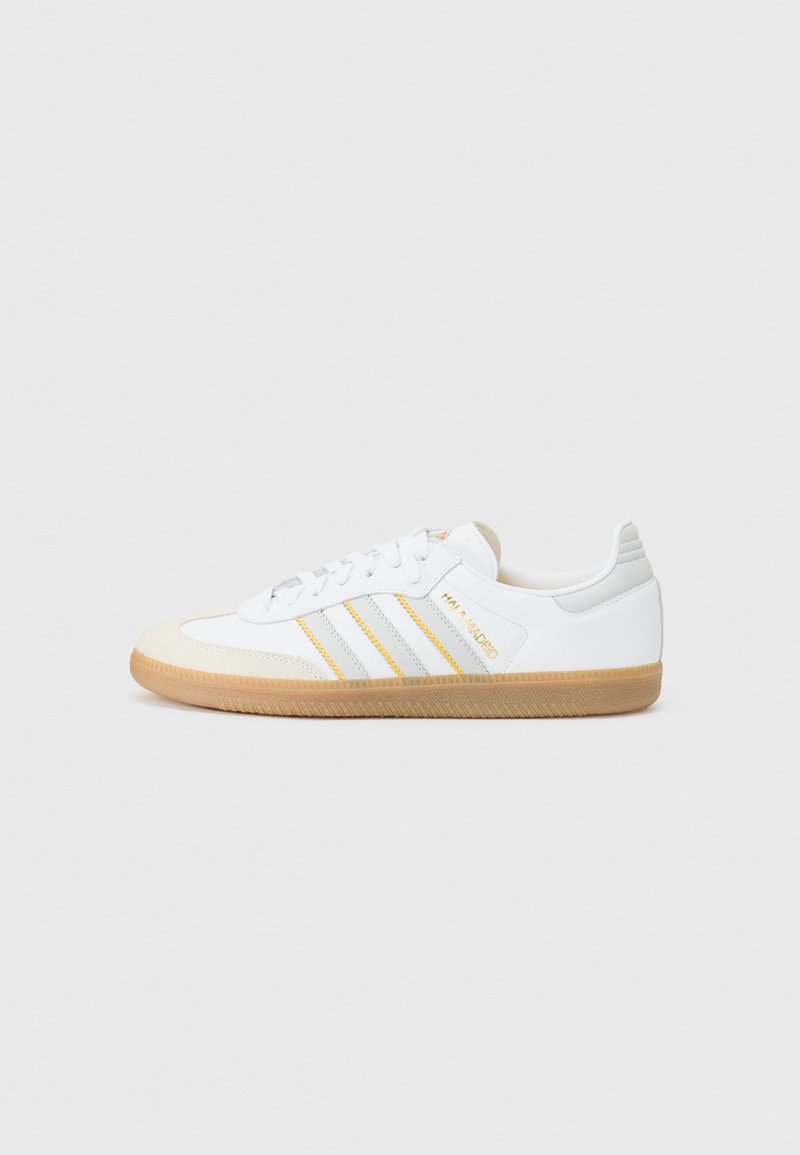 Fehér sneaker három sárga és szürke csíkkal, textúrázott gumi talppal, velúr orral és párnázott sarokkal. Karcsú, alacsony profilos dizájn.