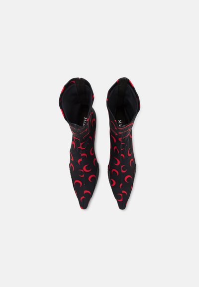 Botines negros con patrones de media luna rojos, hechos de un material elástico. Diseño de punta afilada con una silueta elegante y ajustada.