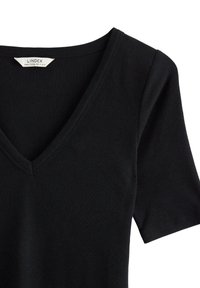 Musta ribbineuloksinen lyhythihainen paita, jossa on V-kaula-aukko ja pehmeä pinta. Merkki näkyy kaula-aukon kohdalla.