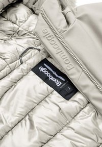 Lichtbeige geïsoleerde jas interieur, met doorgestikte vulling, een gladde buitenlaag en een zwart label met merklogo en maat.