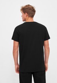 T-shirt en coton noir avec un col ras du cou classique et des manches courtes, présentant une coupe décontractée et un ourlet droit, porté à l'envers.