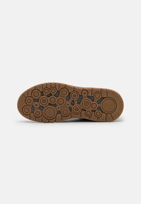 Semelle d'une chaussure marron avec des motifs circulaires et le nom de la marque Geox visible en dessous.