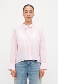 Light pink button-up shirt with a collar and long sleeves, featuring a subtle pattern of small dots and a cropped hemline.
