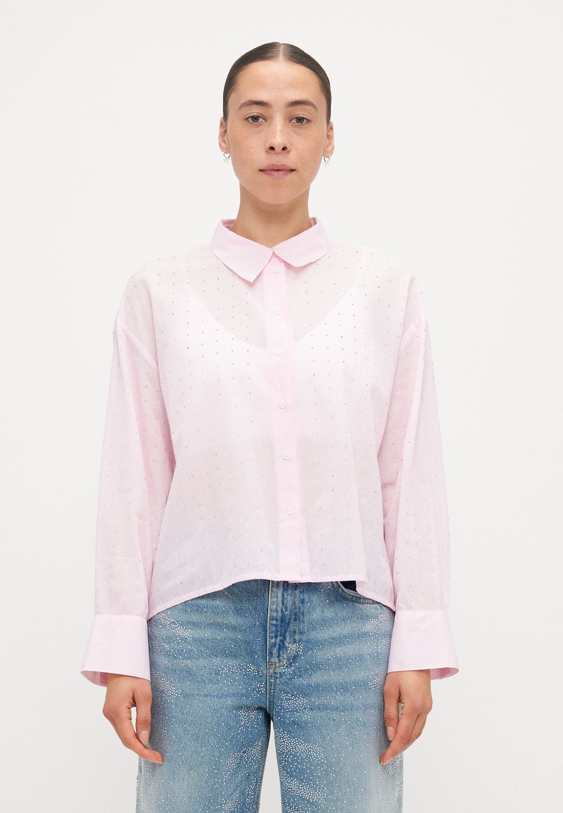 Light pink button-up shirt with a collar and long sleeves, featuring a subtle pattern of small dots and a cropped hemline.