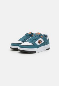 Sneaker turchesi e bianchi con tomaia in pelle e rete, dotate di punta perforata, dettagli neri e un logo arancione sul lato. Suola in gomma.
