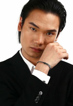 Bracciale con collegamenti in metallo argento e nero; presenta un accento arancione. Indossato su un polso con un abito nero e una camicia bianca.