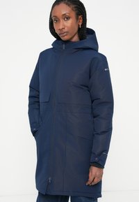 Parka isolante di colore blu navy con chiusura a zip, cappuccio e due ampie tasche frontali. Tessuto liscio con una finitura leggermente lucida.