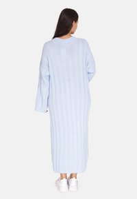 Langes, geripptes Strickkleid in Hellblau, mit Rundhalsausschnitt und langen Ärmeln. Der Stoff hat eine weiche Textur. Kombiniert mit weißen Sneakern.