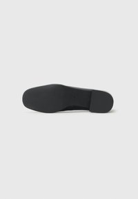 Suola di scarpa nera con superficie texturizzata, tacco leggermente rialzato e bordo liscio. Il materiale appare resistente e flessibile.