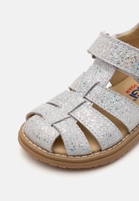 Silberne Glitzersandale mit mehreren Riemen, offenem Zehenbereich und beigefarbener Gummisohle. Sie verfügt über eine weiche Innenauskleidung für zusätzlichen Komfort.