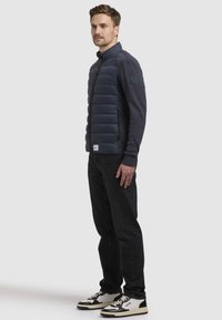 Navy quilted vest med høj krave, puffer sektioner og strikkede ærmer. Parret med sorte jeans og sort-hvide sneakers.