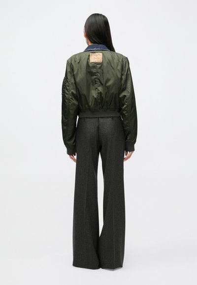 Olijfgroene bomberjack met een geribde zoom, denim kraag en een patchdetail aan de achterkant, gecombineerd met wijd uitlopende broek met krijtstreep.