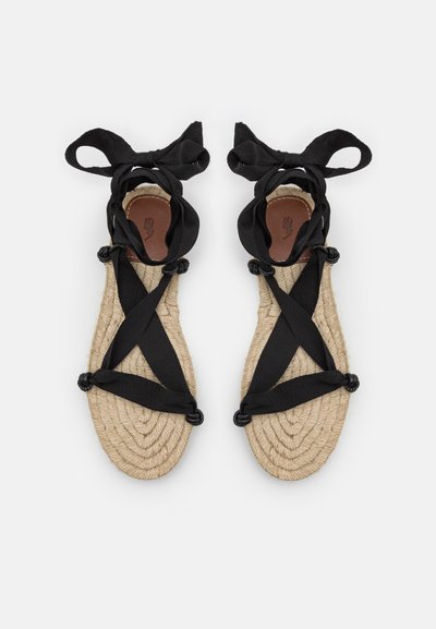 Μαύρες ανατομικές σαγιονάρες με υφασμένο σόλο από τσόχα, που διαθέτουν διασταυρούμενες λωρίδες και στρογγυλά διακοσμητικά. Λείος δερμάτινος πάτος με έμβλημα χεριού.