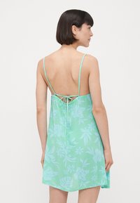 Vestido verde claro con estampado floral, tirantes finos, espalda baja y detalle de lazo. Hecho de una tela suave y transparente, de diseño hasta la rodilla.