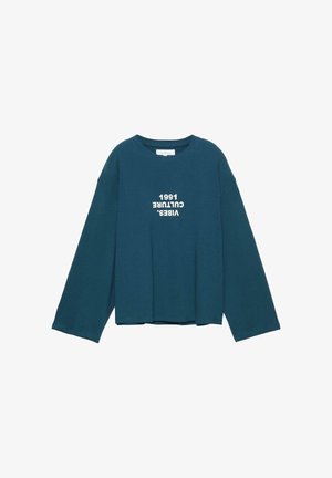 Dolga majica s širokimi rokavi v barvi modrozelene, na sprednji sredini z belim besedilom na glavo: "VIBES. CULTURE 1991".