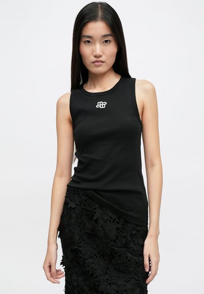 Fekete bordázott ujjatlan felső, kerek nyakkivágással és egy kis fehér logóval a mellkason, egy texturált fekete virágos csipke szoknyával párosítva.