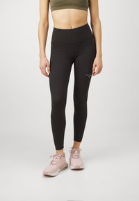 Leggings neri aderenti con vita alta, realizzati in materiale elasticizzato. Abbinati a scarpe da ginnastica rosa chiaro con una finitura testurizzata.