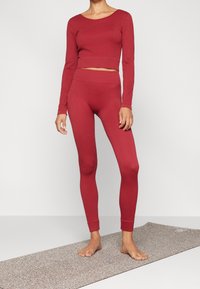 Czerwony, prążkowany, długi top crop i dopasowane legginsy, wykonane z rozciągliwego materiału o miękkiej fakturze, prezentowane na modelce boso.