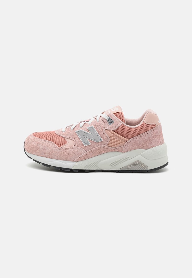 Baskets roses New Balance avec panneaux en suède et mesh, lacets blancs et semelle rembourrée avec semelle extérieure noire, vue de côté sur fond blanc.