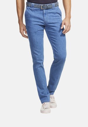 Pantalons en denim bleu clair avec une coupe droite, dotés de passants de ceinture et d'une fermeture éclair, associés à des baskets blanches. Texture lisse, design minimal.