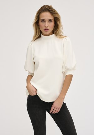 Hvid, højhalset bluse med korte, puffede ærmer, lavet af blødt stof; båret med sorte slim-fit jeans. Glat tekstur, minimalistisk design.