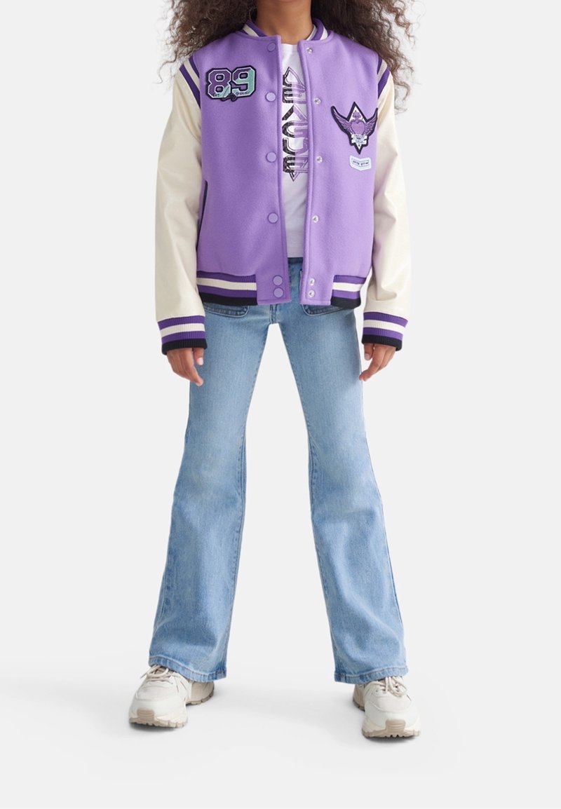Purple varsity jacket with cream sleeves, striped cuffs, and embroidered patches. Worn over a white shirt and paired with light blue jeans.