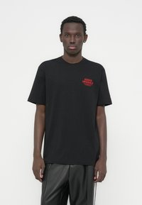 Μαύρο βαμβακερό t-shirt με κοντά μανίκια, με κόκκινο λογότυπο "ADIDAS ORIGINALS" στην αριστερή πλευρά του στήθους. Κλασικός λαιμός τύπου crew neck.