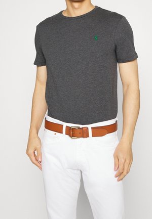 Szara koszulka z krótkim rękawem z zielonym logo, noszona z białymi dżinsami i brązowym skórzanym paskiem z metalową klamrą.