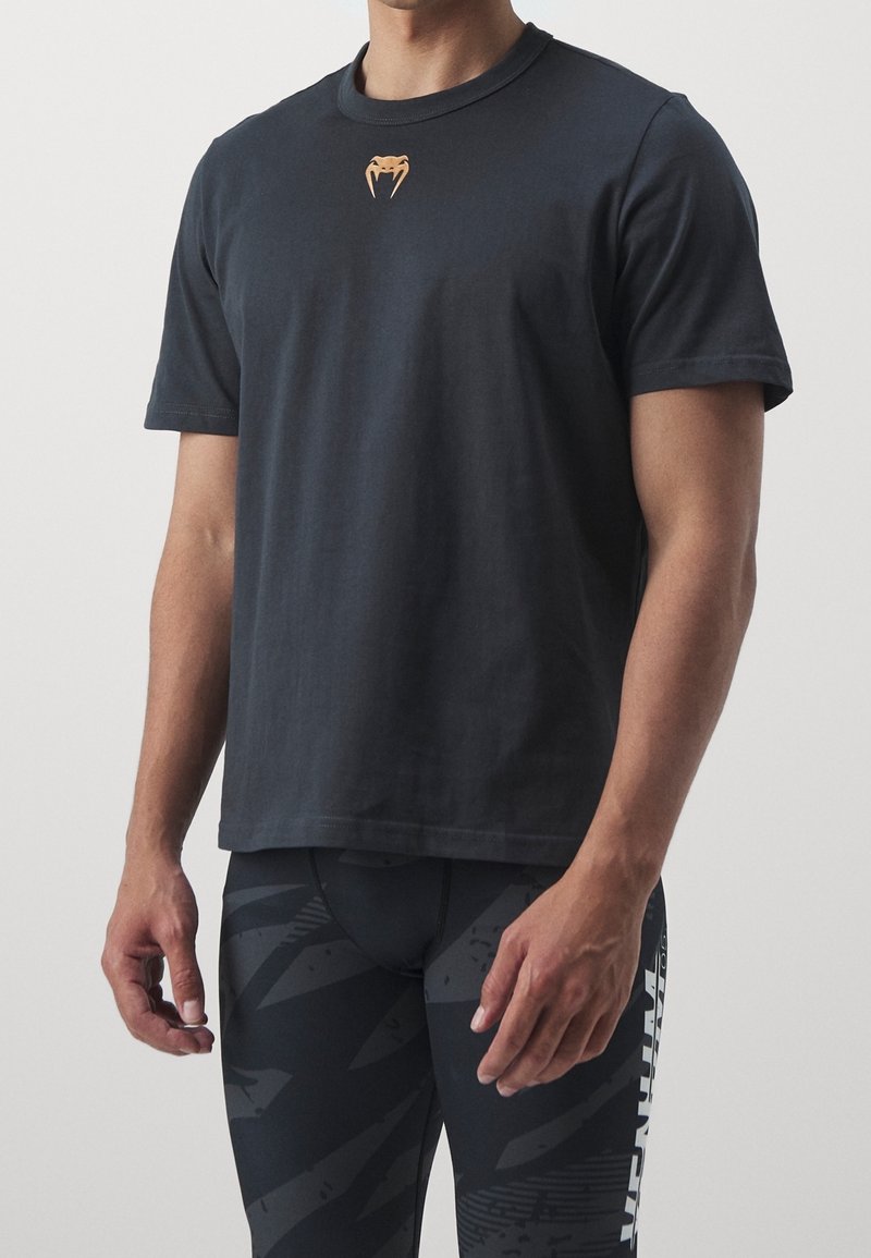 Czarna koszulka z krótkim rękawem z bawełny, z małym pomarańczowym logo na klatce piersiowej. Połączona z czarnymi legginsami sportowymi w wzory.