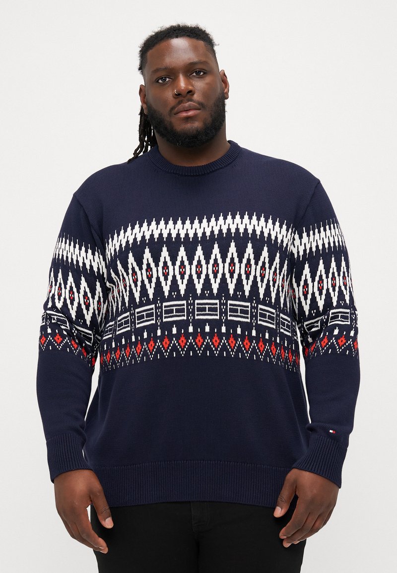 Navy knitted sweater featuring a geometric white and red pattern across the chest, with ribbed cuffs and hem.