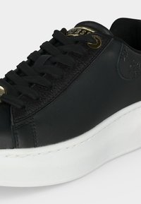Μαύρο δερμάτινο sneaker με παχύ λευκό πάτο, μαύρα κορδόνια και χρυσά μεταλλικά κουμπώματα και λογότυπο στη γλώσσα.