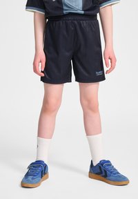 Svarta sportshorts med ett texturerat randmönster, utrustade med ett elastiskt midjeband och en blå logotyp, tillsammans med blå sneakers och vita strumpor.