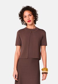 Bruine top met korte mouwen en een ronde halslijn, voorzien van een voorkluit en een sluitdetail. De stof lijkt glad en heeft een gestructureerde pasvorm.