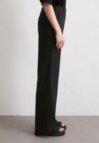 Zwarte wijde broek met een gladde textuur, een hoge taille en subtiele zijzakken. Combinatie met gestructureerde zwarte sandalen.