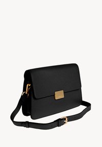 Sac à bandoulière en cuir noir avec fermeture à rabat, quincaillerie dorée et bandoulière amovible. Présente une surface texturée et un design minimaliste.