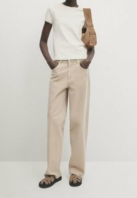 Beige leveled trousers, valkoiset lyhythihaiset paidat, ruskea olkotasku, ja remmit ruskeat sandaalit. Sujuva kangas, minimalistinen muotoilu.